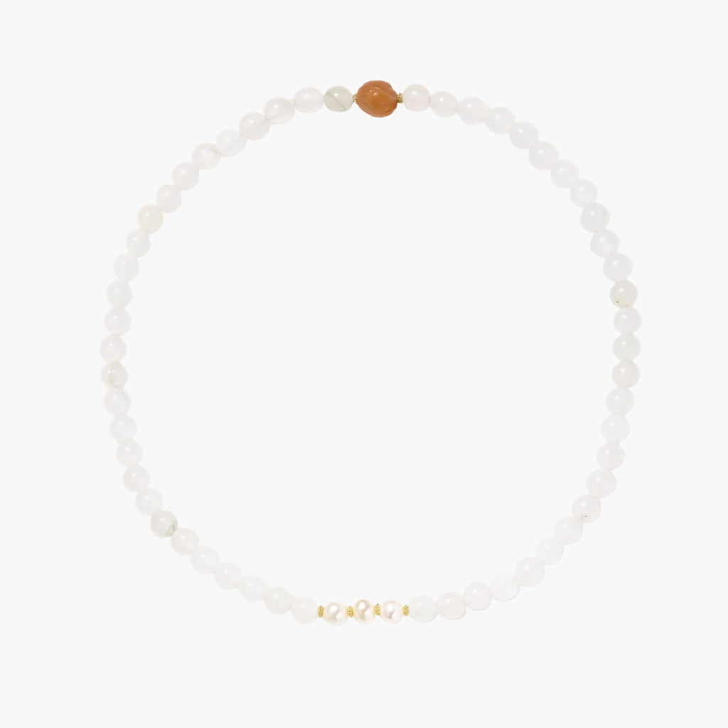 Three layered white beaded bracelets with carved orange agate lotus centerpiece and freshwater pearls on cream background.