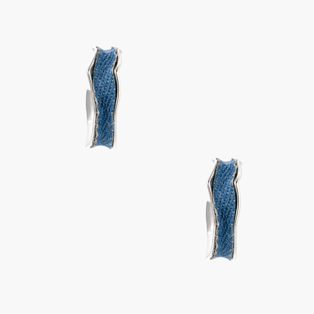 Silver huggie hoops with blue denim fabric inlay strip and polished white gold plated finish on cream background.
